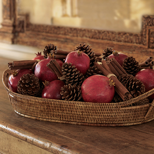 Pomegranates, cinnamon stick bundles, and pinecones in a low woven basket.